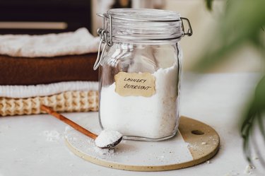 Glass jar of natural laundry detergent and a wood spoon, on a round cutting board